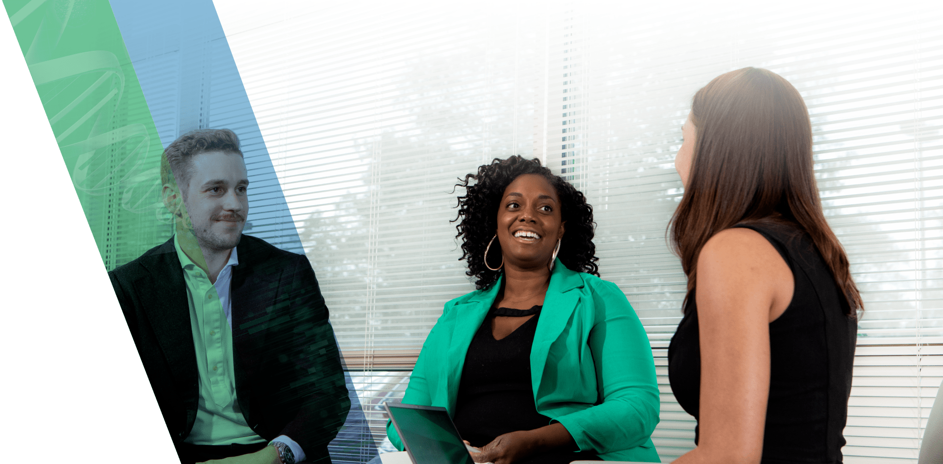 Three professionals sit at a table in an office, smiling at one another.
